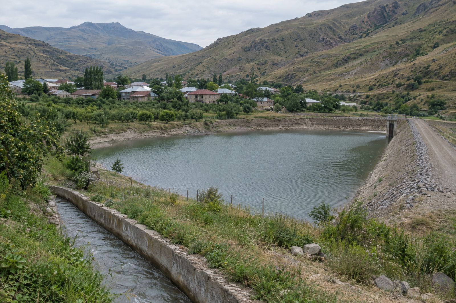 Small reservoir embankment beside a village and irrigation channel